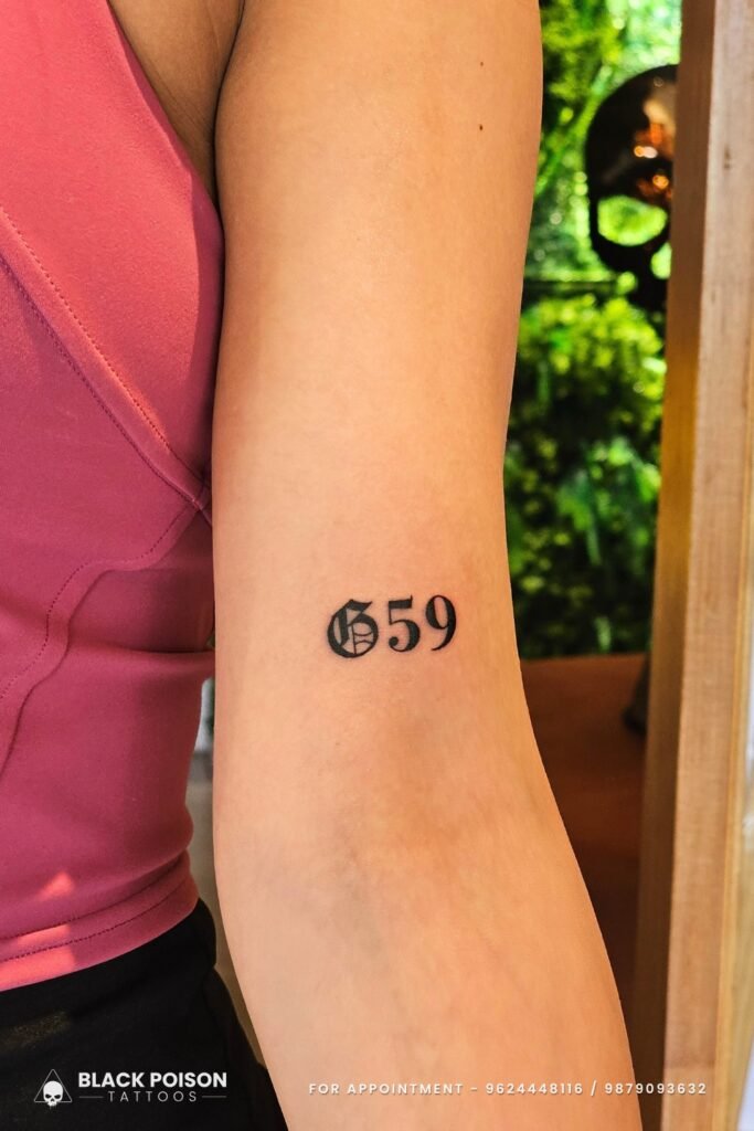 G59 blackwork lettering tattoo on inner tricep - minimalist music tribute