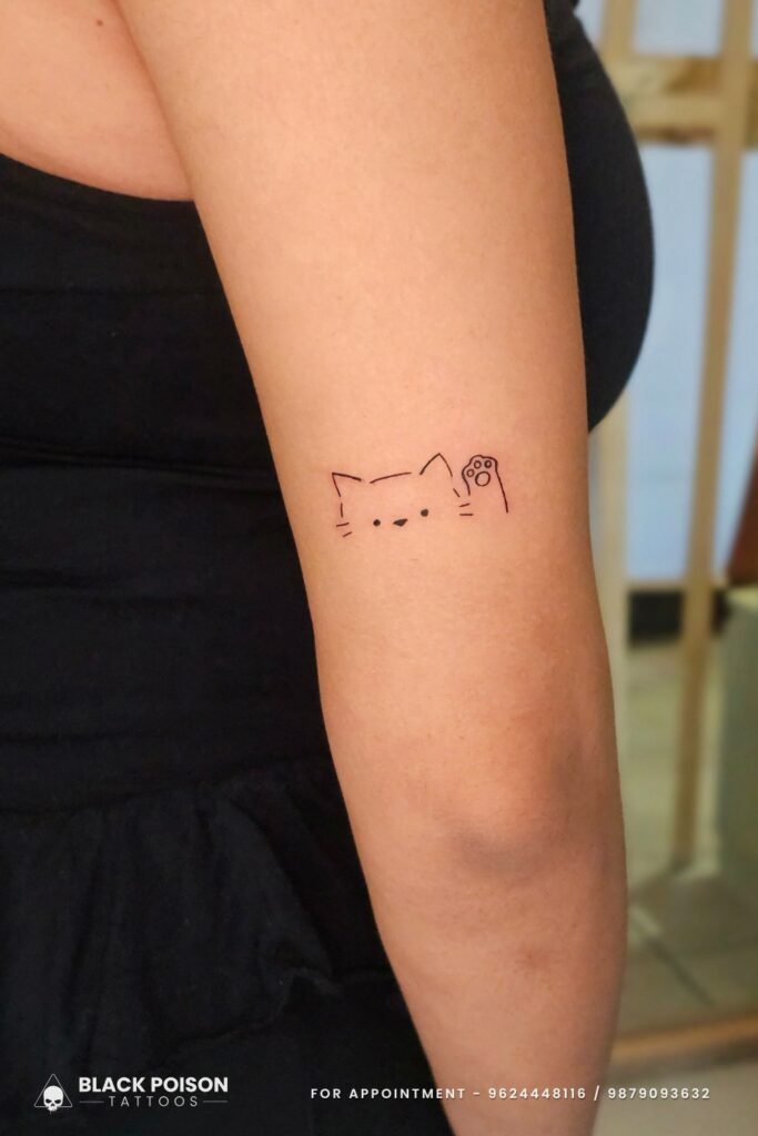 Minimal fine line cat tattoo with paw on upper arm by Black Poison Tattoos Ahmedabad