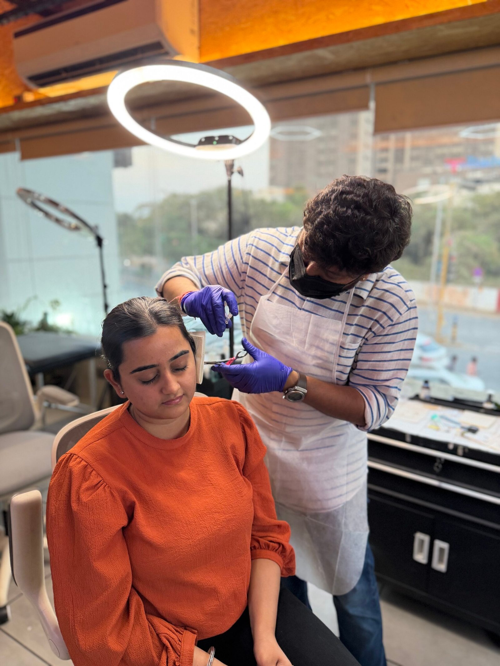 Professional piercer wearing sterile gloves and a mask performing a safe ear piercing procedure on a client at Black Poison Tattoos Ahmedabad.