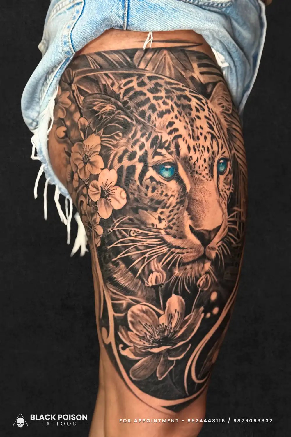 Black and grey realistic leopard tattoo with blue eyes and flowers on the thigh, done at Black Poison Tattoos in Ahmedabad.