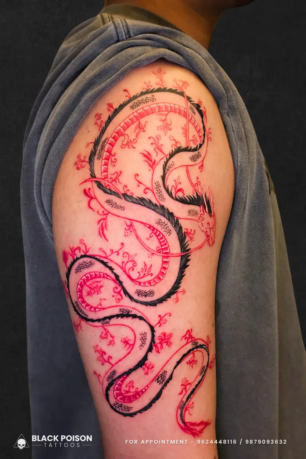 Striking red and black fine line Asian dragon tattoo with floral accents on the upper arm done at Black Poison Tattoos in Ahmedabad.