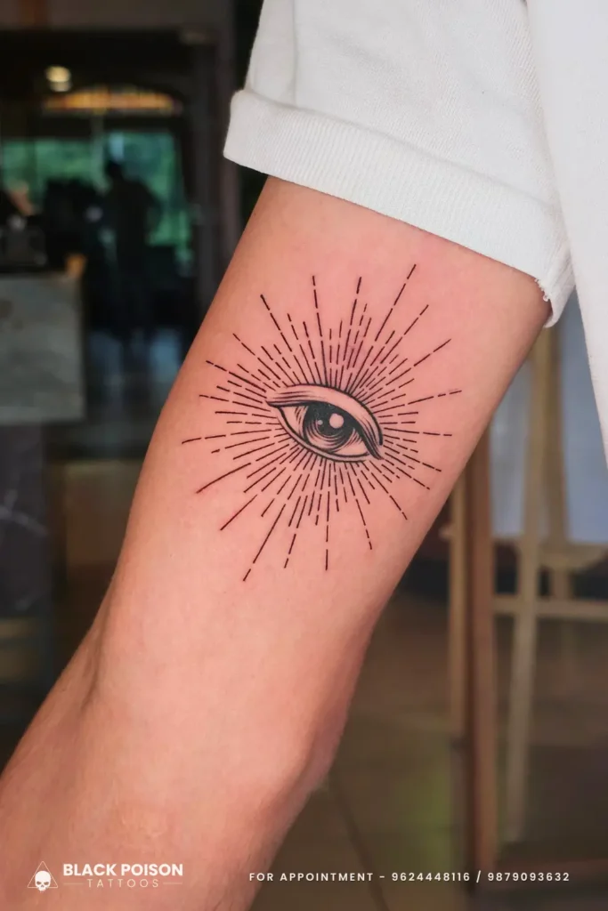 A detailed fine line evil eye tattoo with a geometric sunburst radiance on the inner bicep by Black Poison Tattoo Studio Ahmedabad.