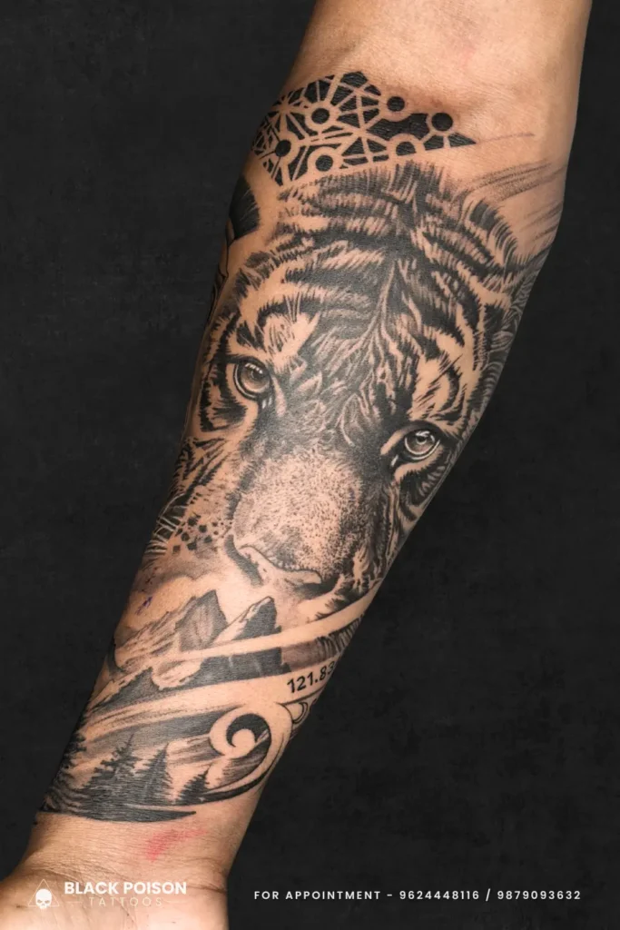 Detailed black and grey realism tattoo of a tiger's face merging with a forest mountain landscape and geometric patterns on a forearm.