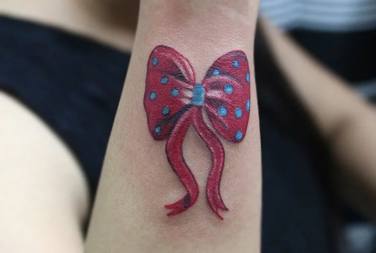 Colour ribbon bow tattoo with red and blue polka dots on the arm