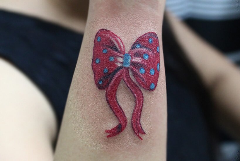 Colour ribbon bow tattoo with red and blue polka dots on the arm