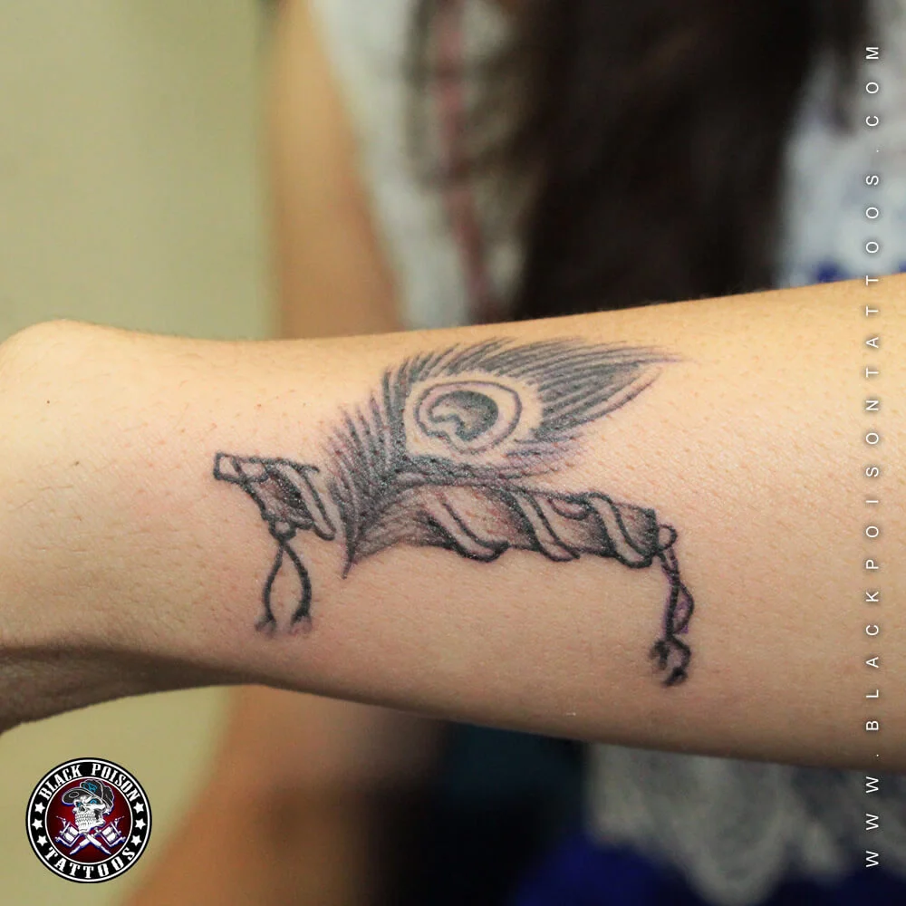 Black and grey peacock feather and flute tattoo on the forearm