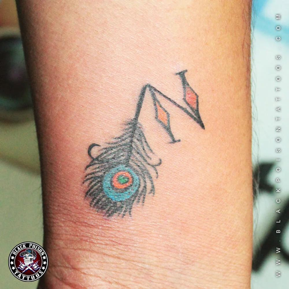 Small peacock feather tattoo with a letter N on the wrist