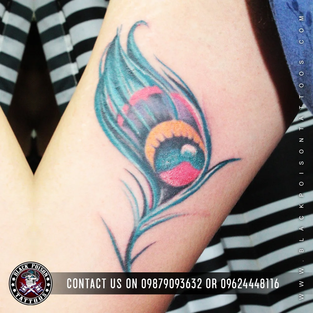 Vivid teal and pink peacock feather tattoo on the inner arm