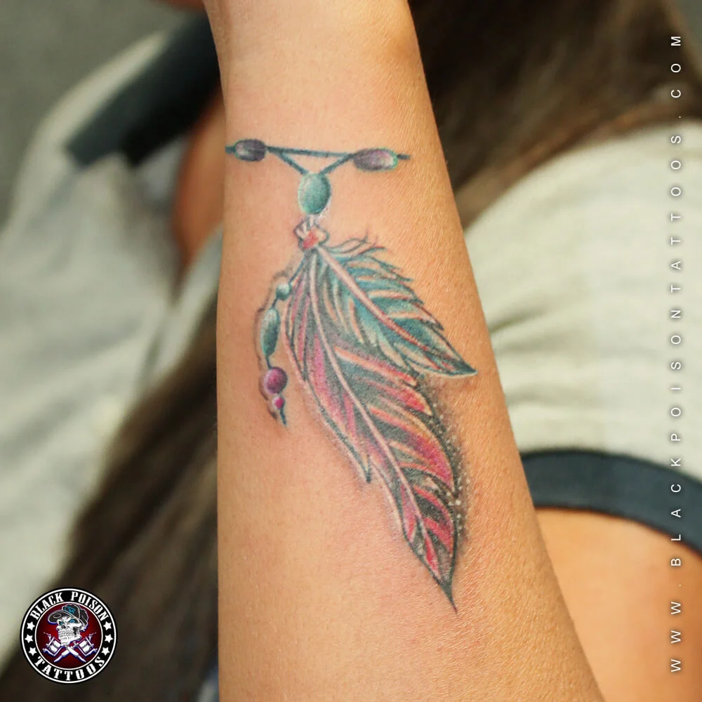 Two colourful hanging feather tattoos in green and pink on the arm