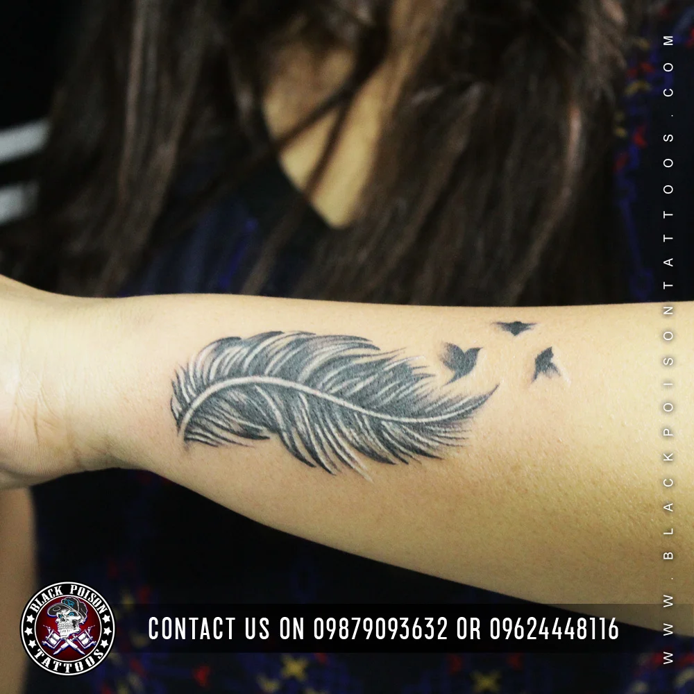 Black and grey feather tattoo with small birds flying from it on the forearm