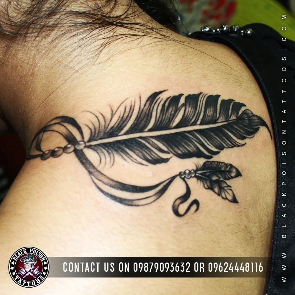 Large black and grey feather tattoo with a hanging charm on the shoulder