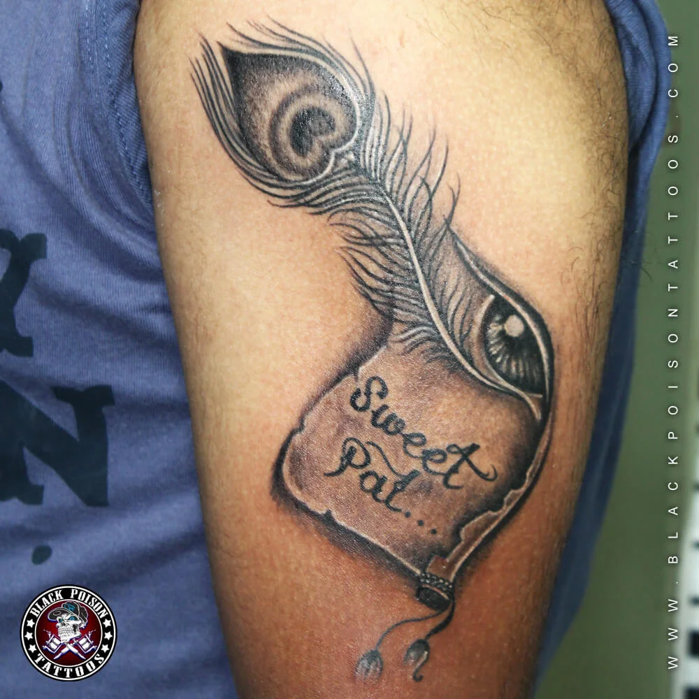 Large peacock feather tattoo with a Sweet Pal banner on the upper arm