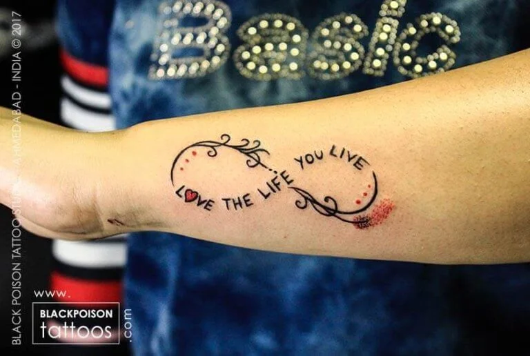 Infinity ribbon tattoo with the words love the life you live on the forearm
