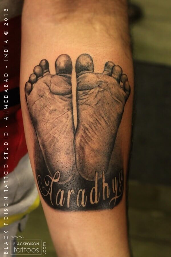 Realistic baby footprints tattoo with a name in script on the forearm