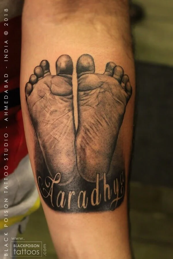 Realistic baby footprints tattoo with a name in script on the forearm