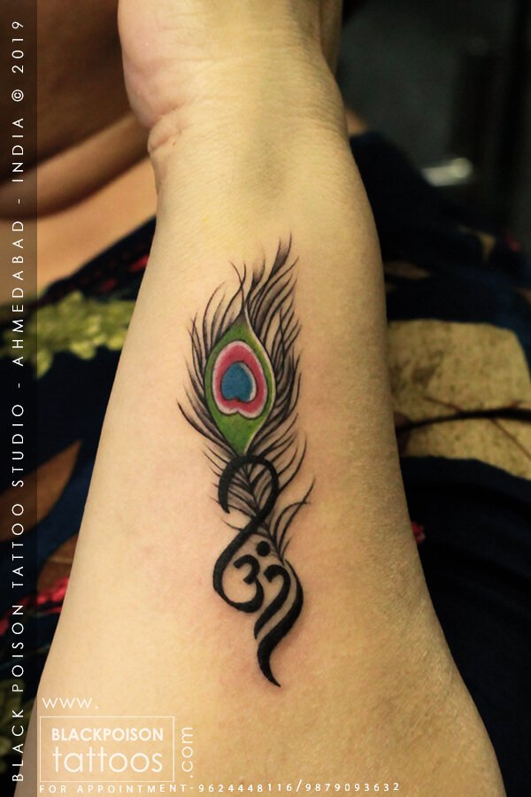 Peacock feather tattoo in colour with an Om symbol at the base on the forearm by Black Poison Tattoo Studio Ahmedabad