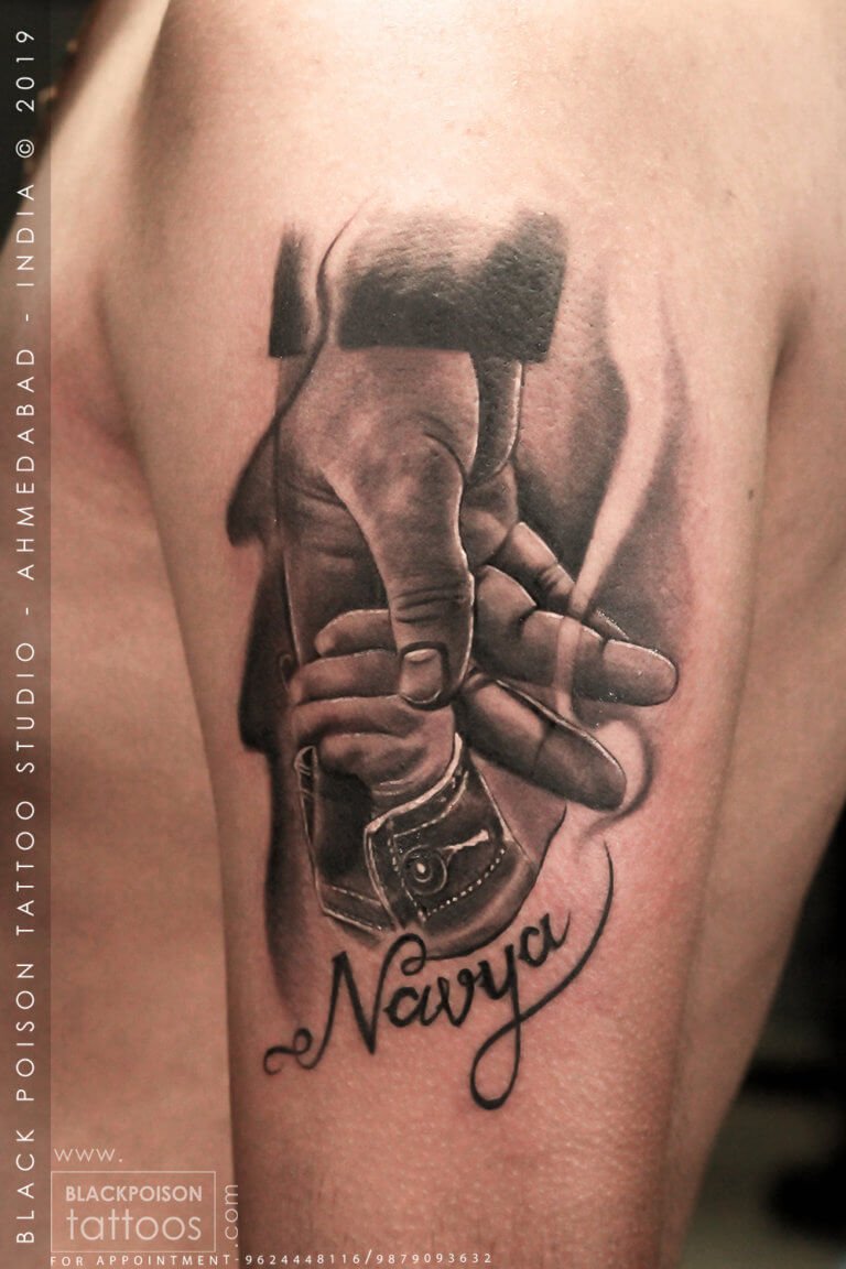Realistic father and daughter tattoo of an adult hand holding a baby hand with a name in script by Black Poison Tattoo Studio Ahmedabad