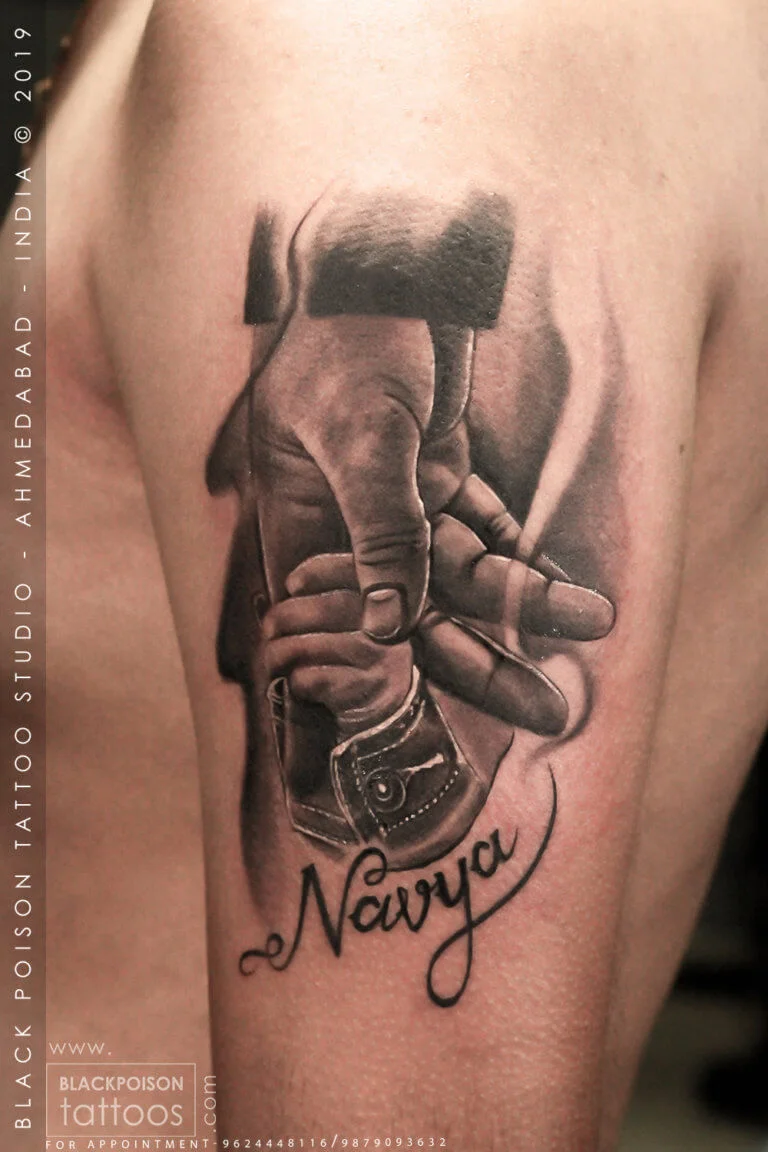 Realistic father and daughter tattoo of an adult hand holding a baby hand with a name in script by Black Poison Tattoo Studio Ahmedabad