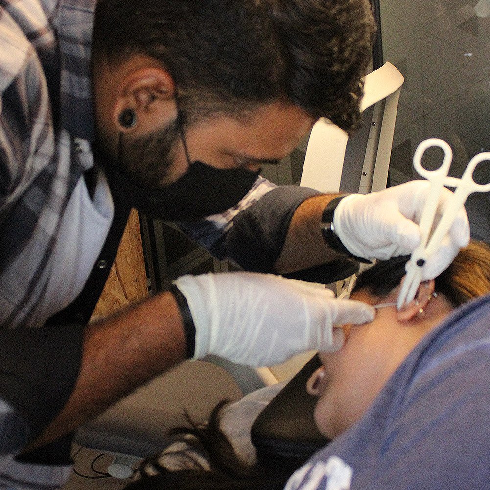 Piercer using a piercing clamp on a client's ear at the studio