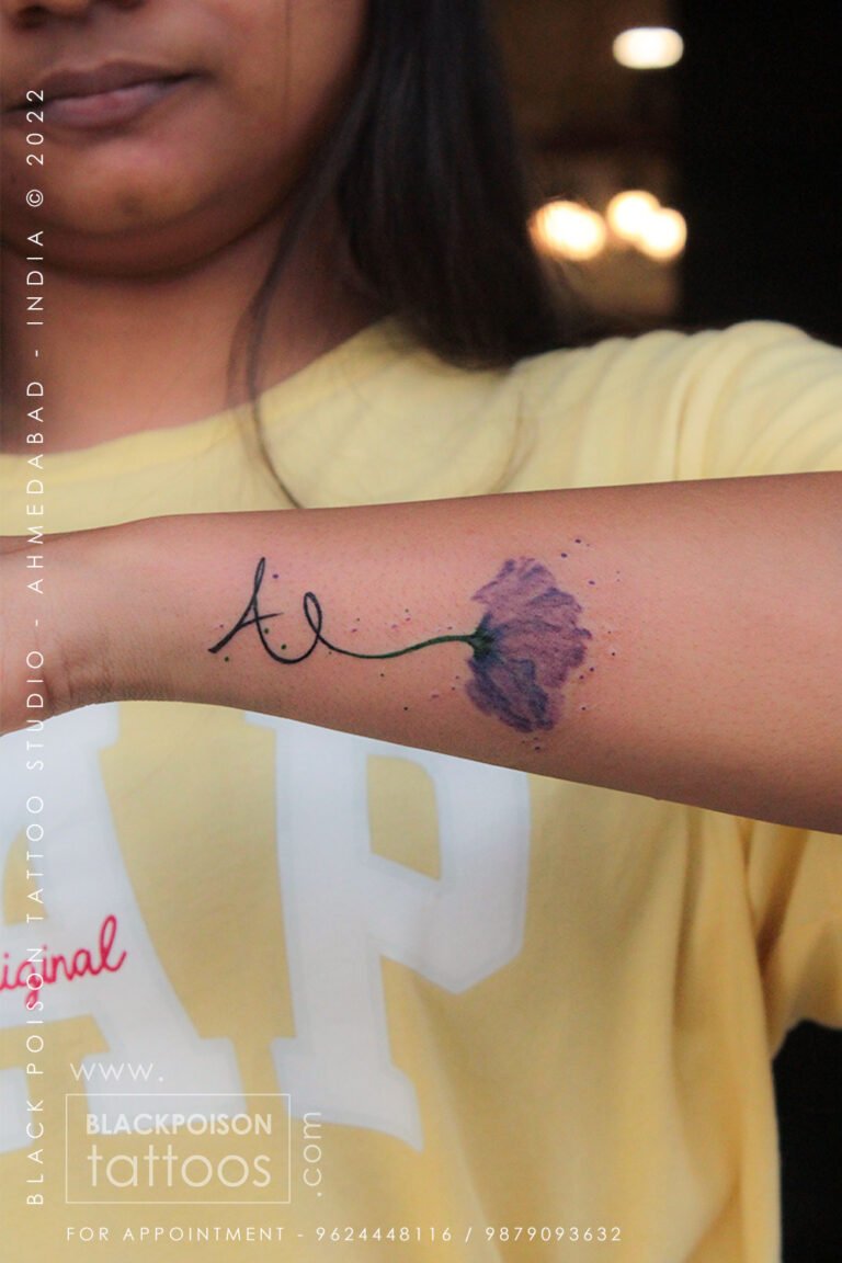 Fine line letter A tattoo joined to a purple watercolour flower on the forearm