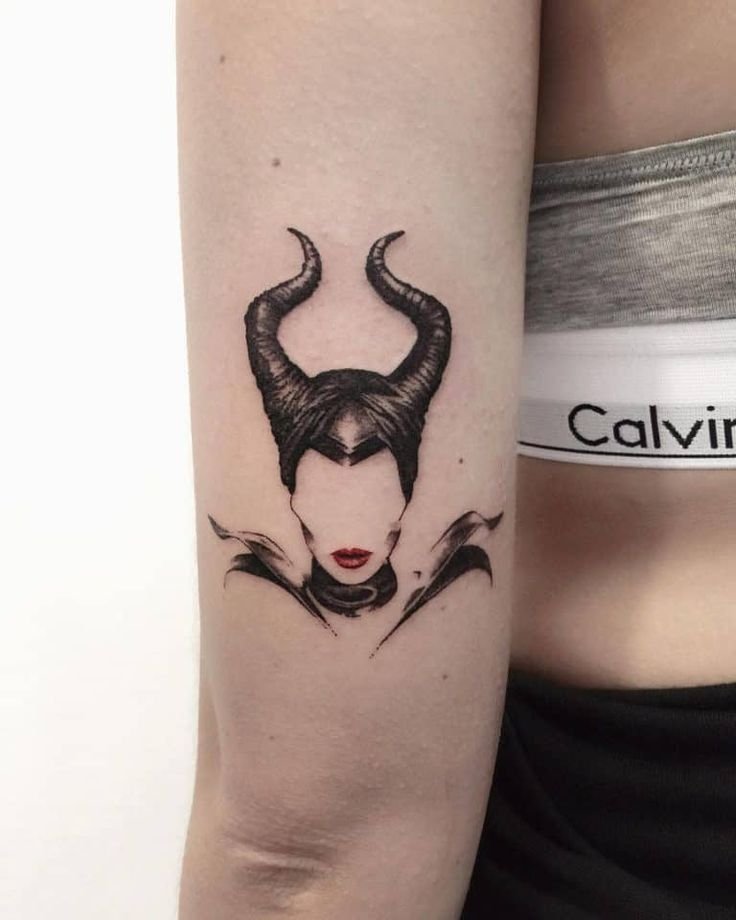 Black and grey Maleficent tattoo with horned headdress and red lips on the forearm