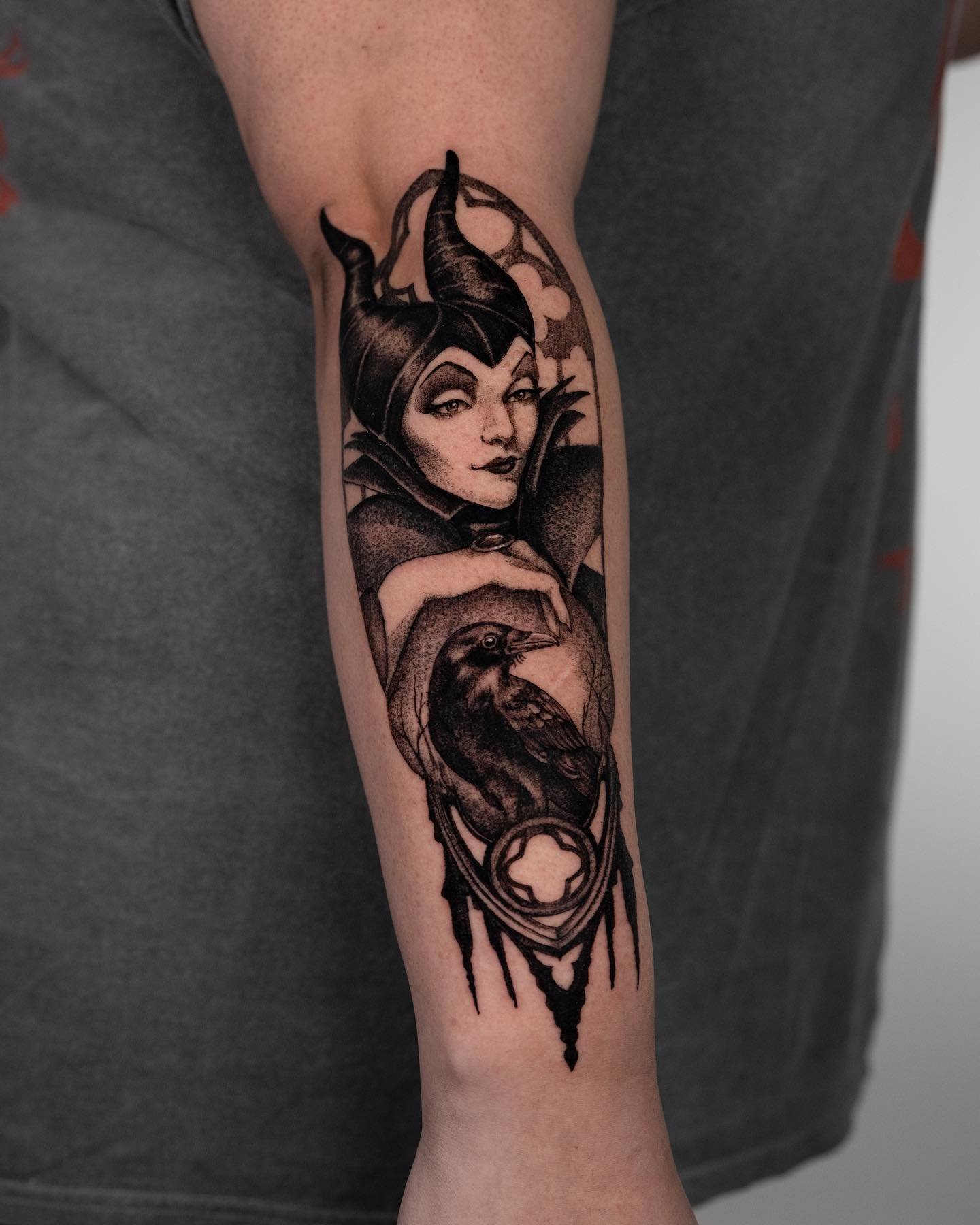 Black and grey Maleficent and raven forearm tattoo with ornamental detail