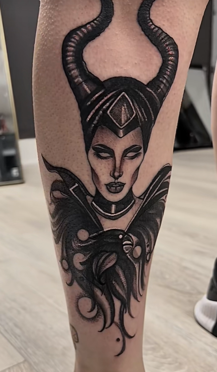 Black and grey Maleficent tattoo with horned headdress and flowing detail on the leg