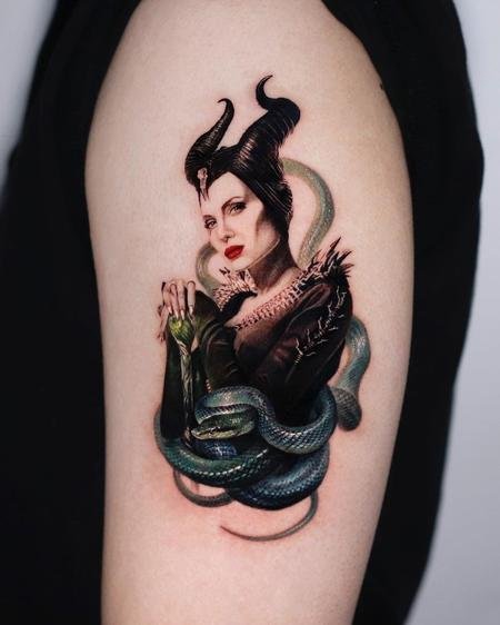 Colour Maleficent tattoo with a green serpent coiled beneath it on the upper arm