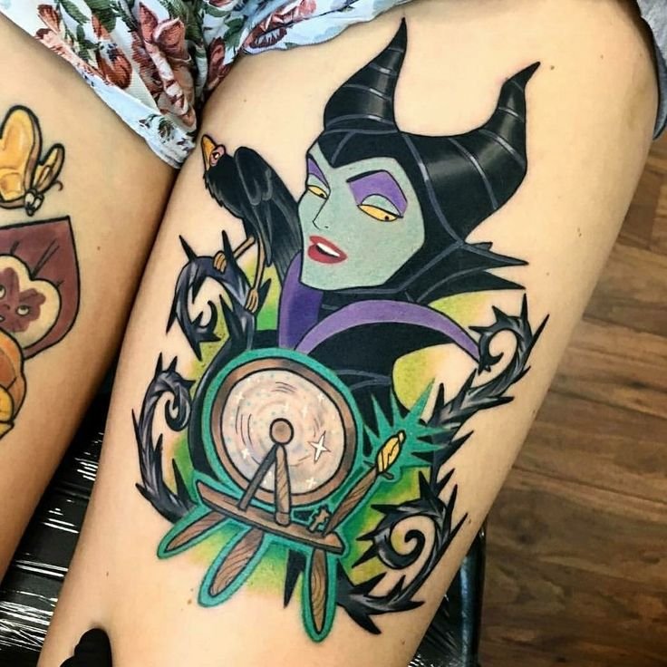 Bright colour cartoon style Maleficent tattoo with a spinning wheel on the thigh