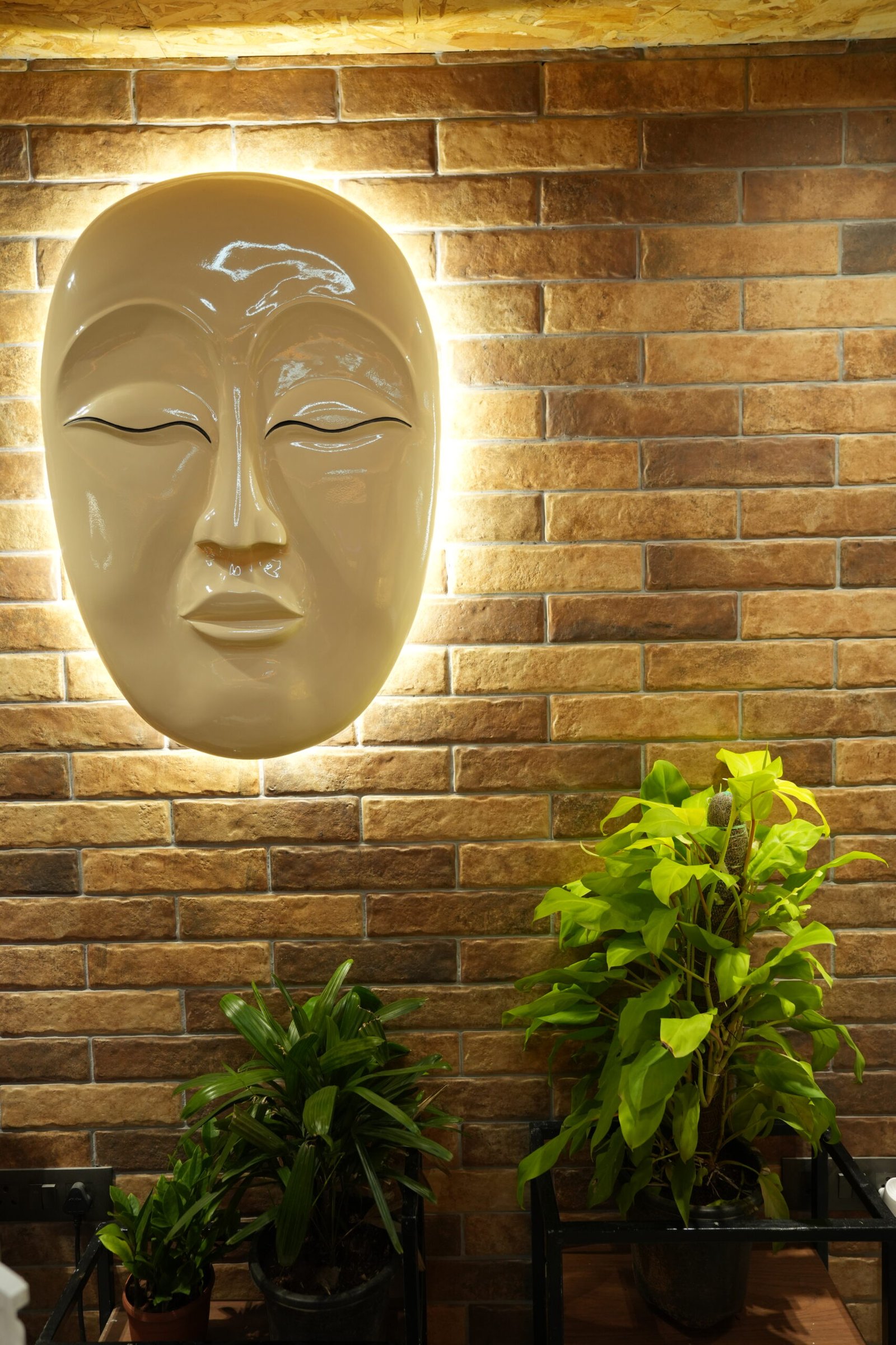 Backlit Buddha face wall sculpture on a brick wall inside the studio
