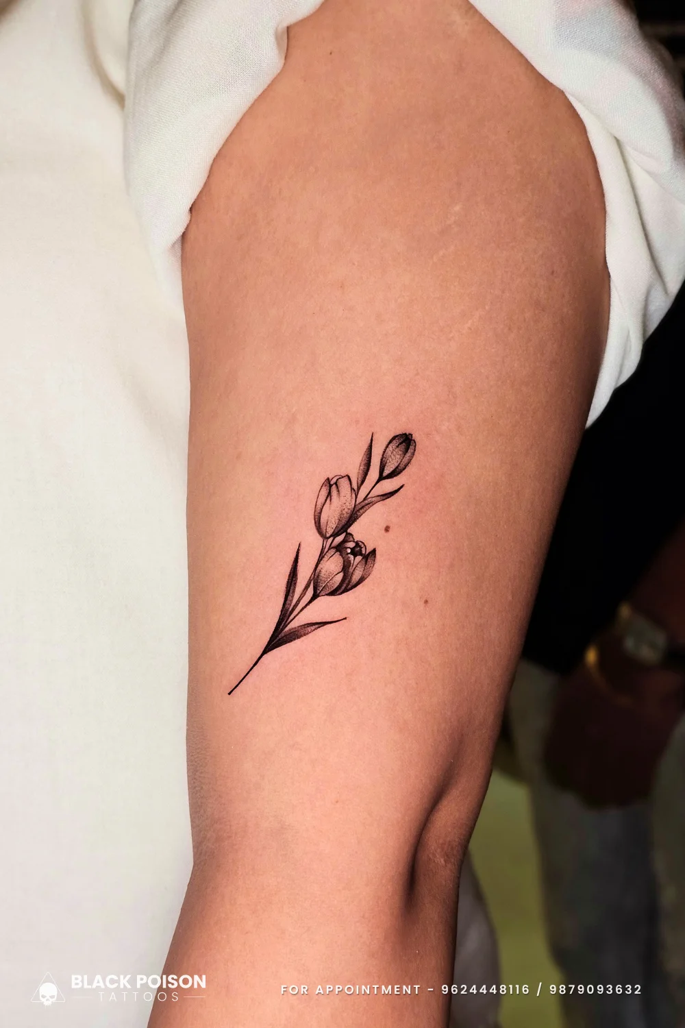 Delicate fine line minimalist tulip flower tattoo on the upper arm done at Black Poison Tattoo Studio in Ahmedabad.