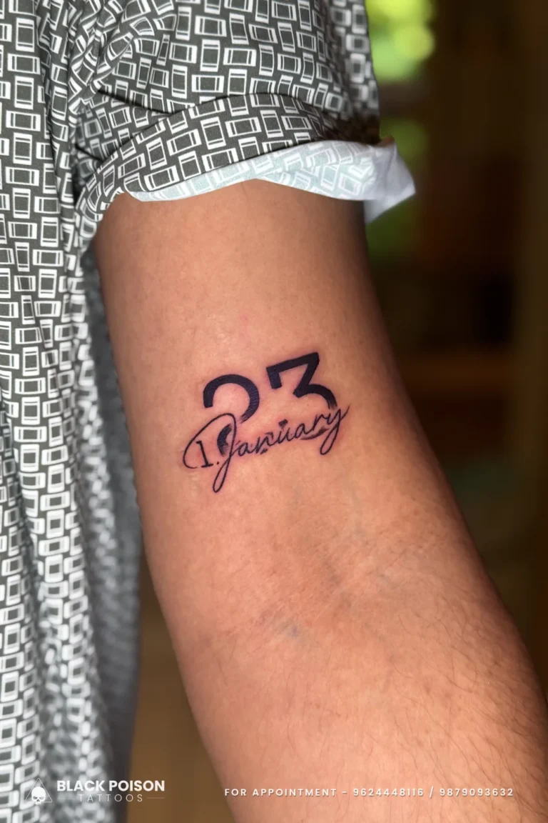 Date tattoo with 23 in bold outlined numerals and January in cursive on the arm at Black Poison Tattoo Studio, Ahmedabad