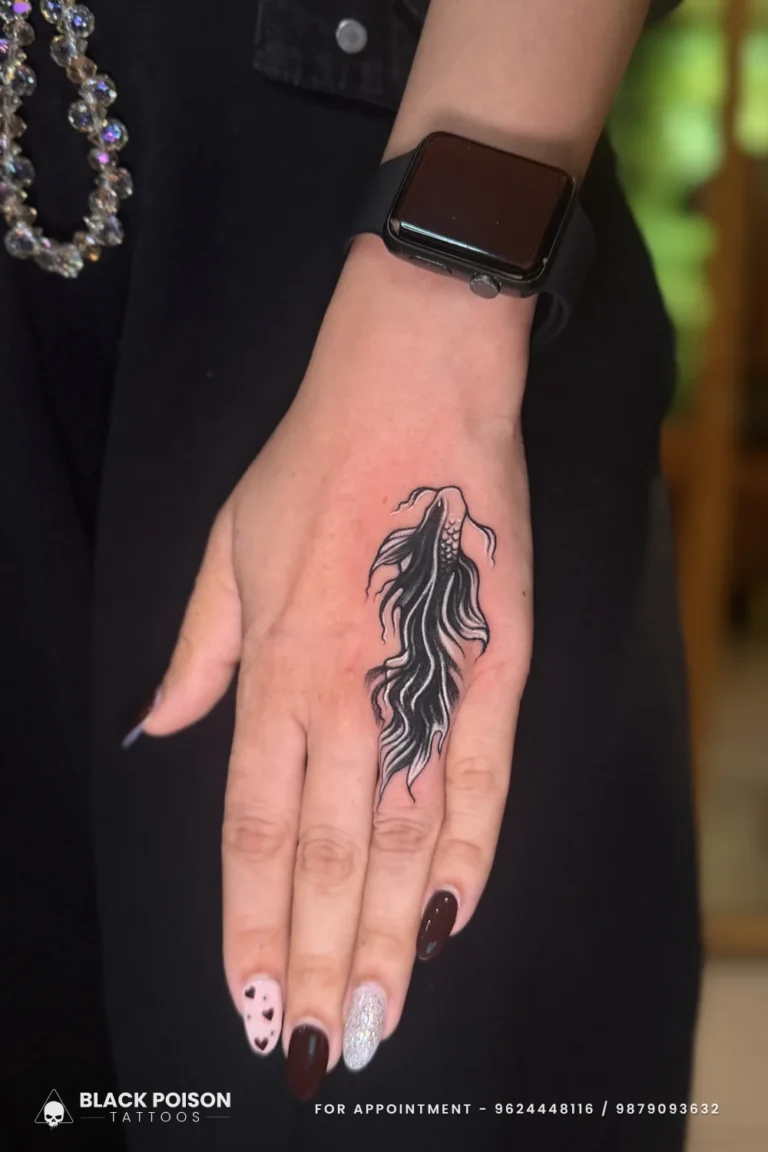 Black and grey betta fish tattoo with flowing fins on the back of the hand at Black Poison Tattoo Studio, Ahmedabad