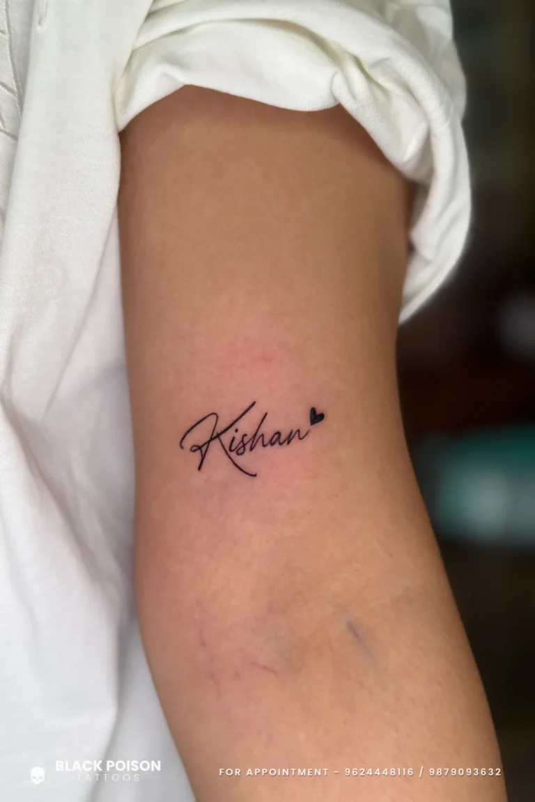 Bold black cursive name tattoo with a small solid heart on the upper arm at Black Poison Tattoo Studio, Ahmedabad