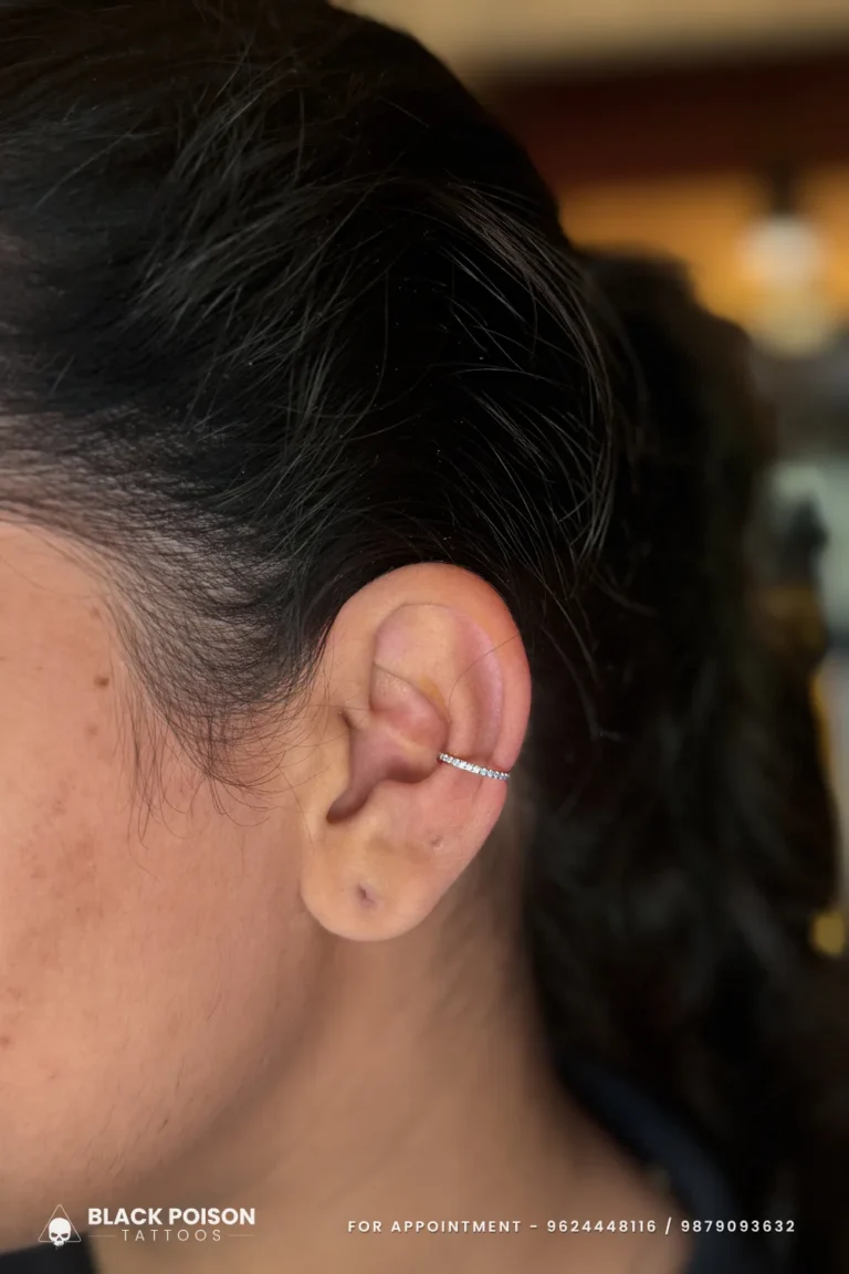 Conch piercing with a slim crystal-set silver ring hugging the inner curve of the ear at Black Poison Tattoo Studio, Ahmedabad
