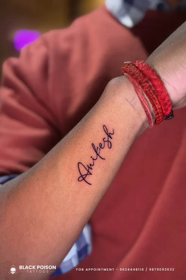 A name in flowing black cursive script tattooed along the inner forearm near the wrist at Black Poison Tattoo Studio, Ahmedabad