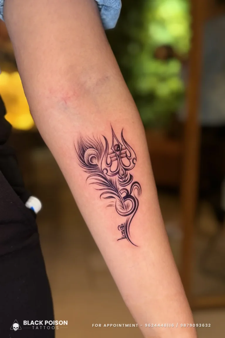 Fine line trishul with an Om at its base and a peacock feather on the forearm at Black Poison Tattoo Studio, Ahmedabad