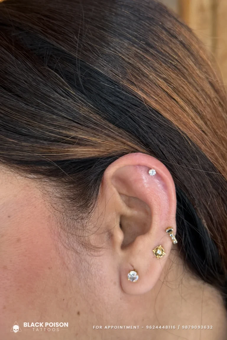 Flat piercing with a crystal stud above a lobe of stacked gold jewelled studs at Black Poison Tattoo Studio, Ahmedabad