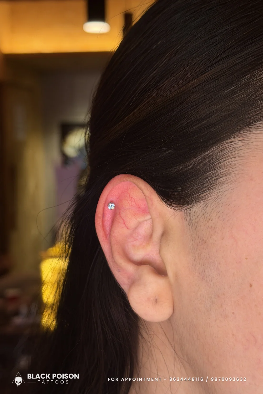 Freshly pierced helix with a small crystal stud on the upper rim of the ear, skin still pink from the piercing