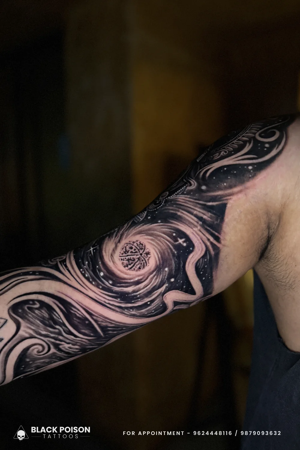 Inner arm view of a black and grey cosmic spiral tattoo with a mandala sphere at the centre and smoke-like swirls