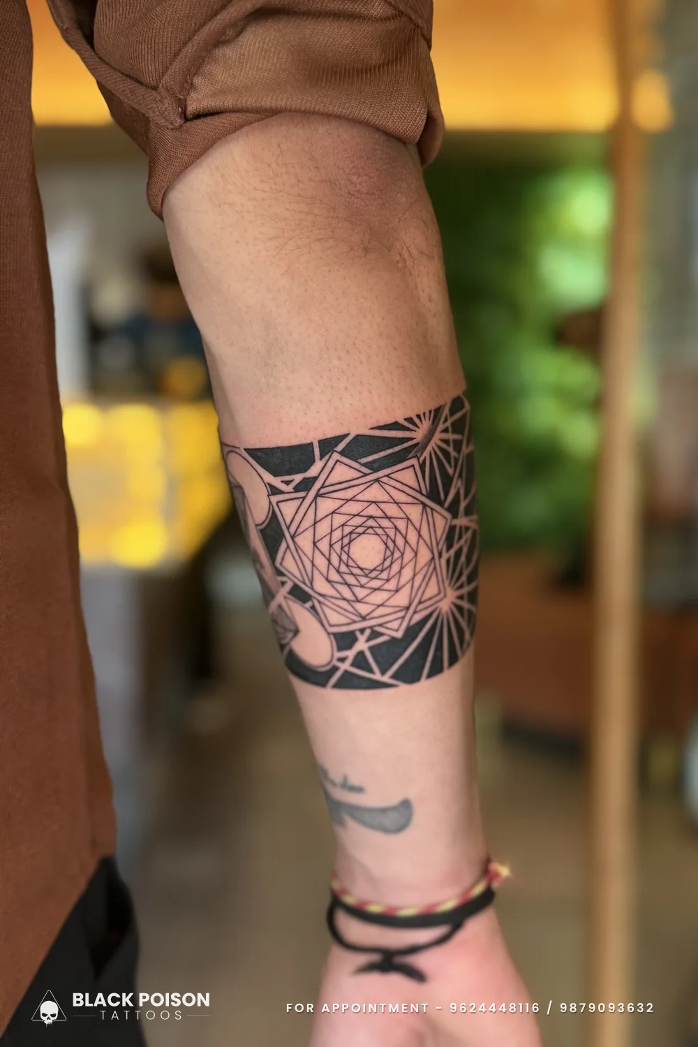 Inner forearm view of a black armband tattoo with a nested hexagonal mandala cut out in negative space