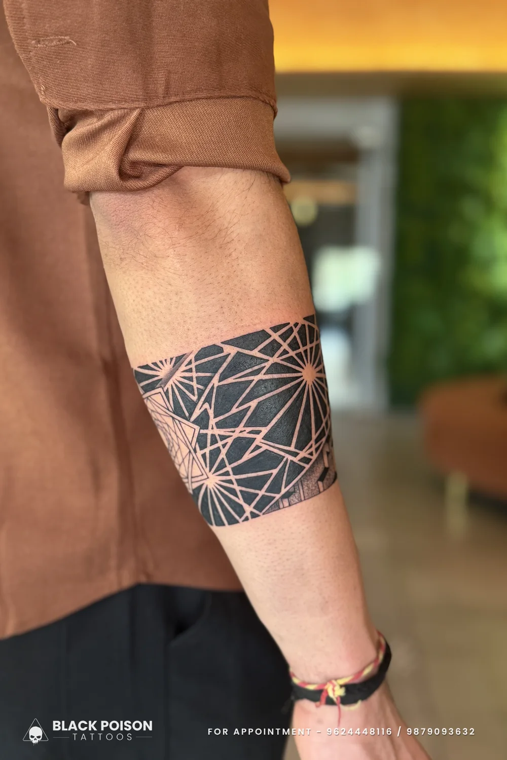 Outer forearm view of a geometric blackwork armband tattoo with negative-space lines fanning across solid black