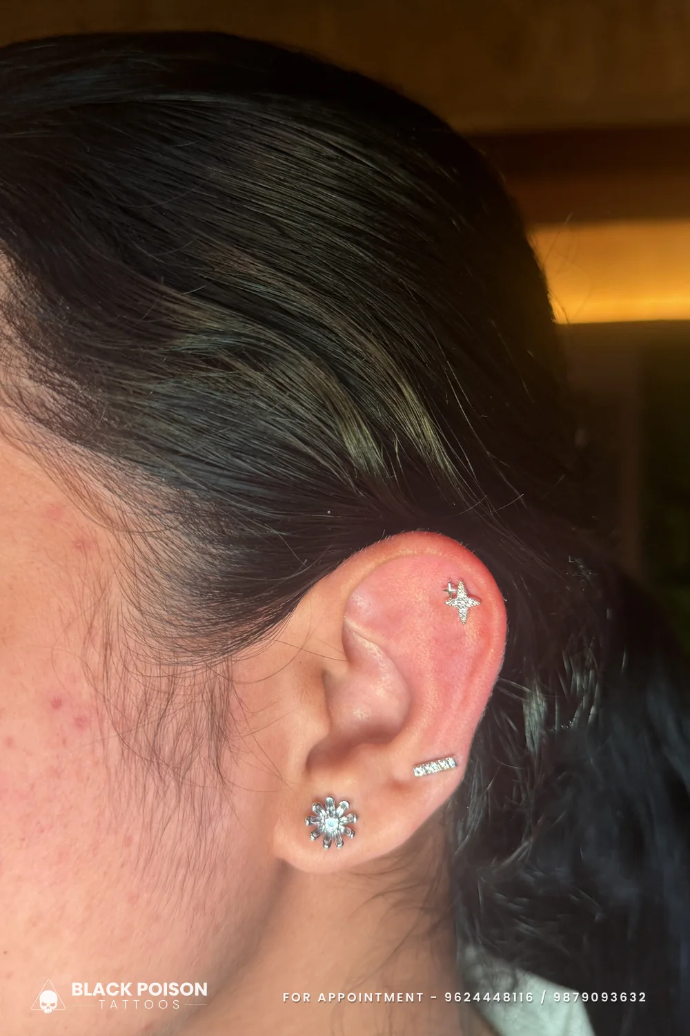 Helix piercing with a four-point star stud, a small jewelled bar lower on the ear and a crystal flower stud on the lobe