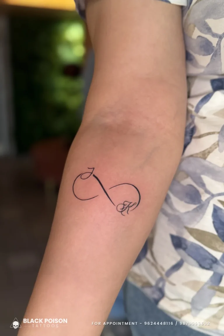 Fine line infinity tattoo with a cursive initial in each loop on the forearm at Black Poison Tattoo Studio, Ahmedabad