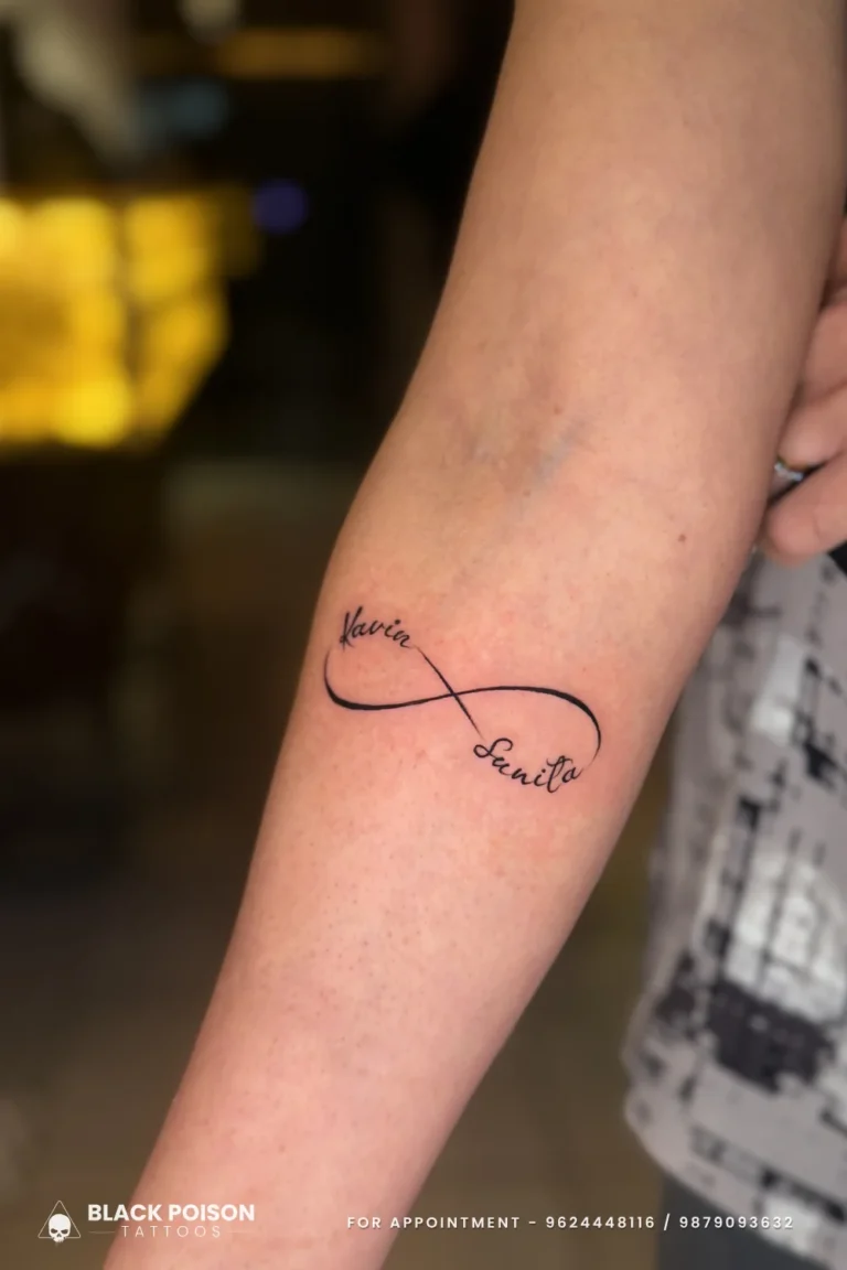 Black infinity tattoo with two cursive names along the loops on the inner forearm at Black Poison Tattoo Studio, Ahmedabad