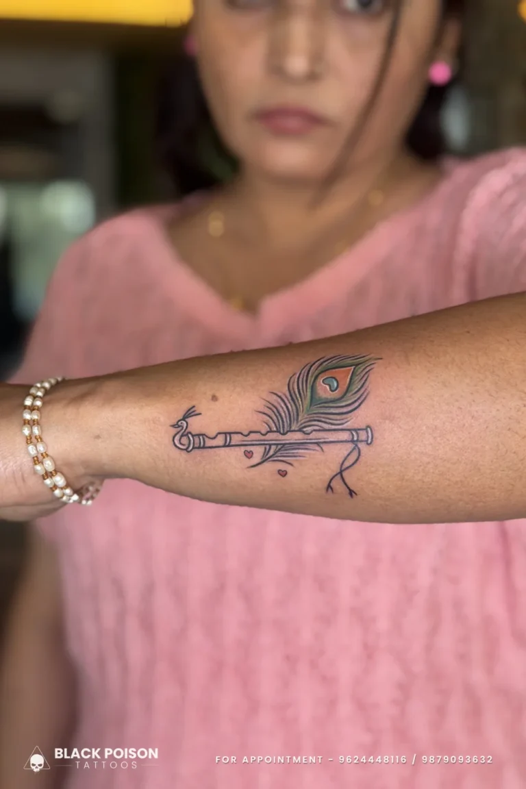 Fine line Krishna flute with a green and blue peacock feather on the inner forearm at Black Poison Tattoo Studio, Ahmedabad