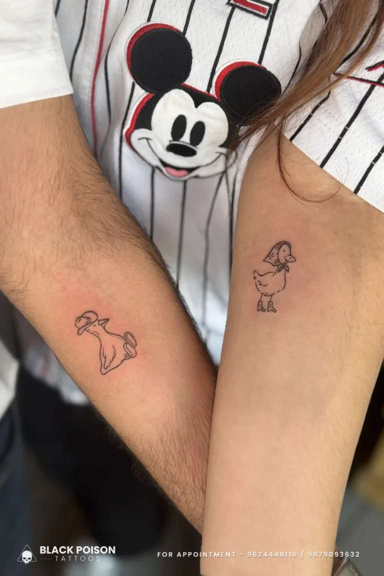 Matching cartoon dog and duck outline tattoos in black ink on two forearms at Black Poison Tattoo Studio, Ahmedabad