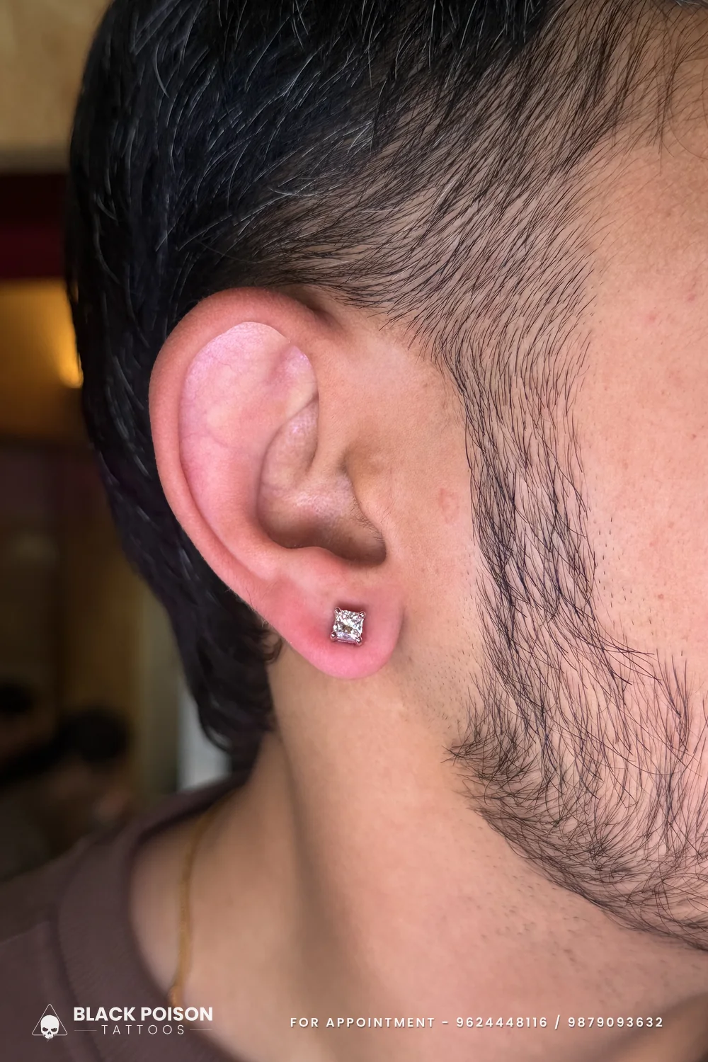 Men's ear lobe piercing with a square princess-cut crystal stud in a four-claw setting, skin slightly pink from the fresh piercing