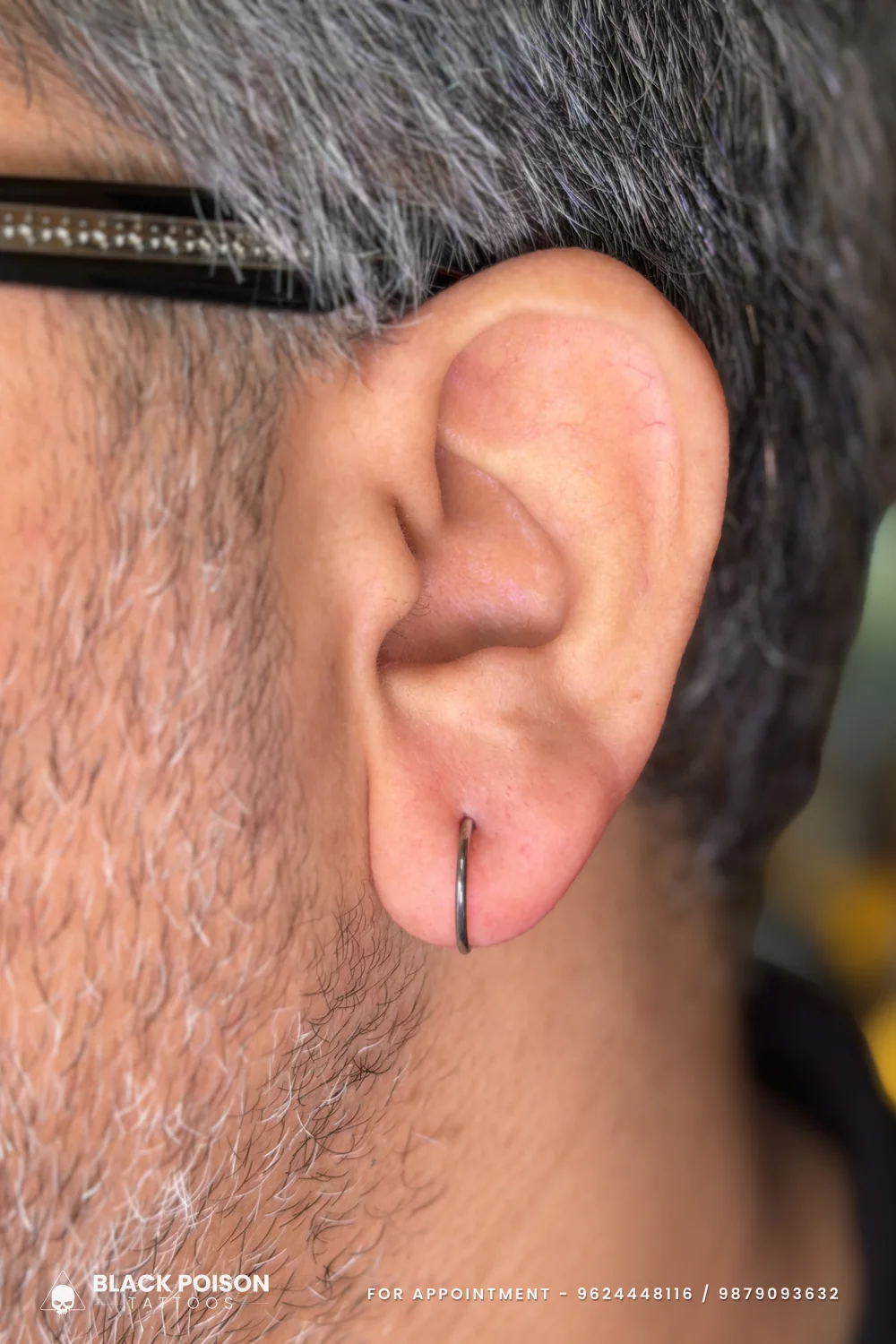 Men's ear lobe piercing wearing a slim black hoop ring that hugs the bottom edge of the lobe