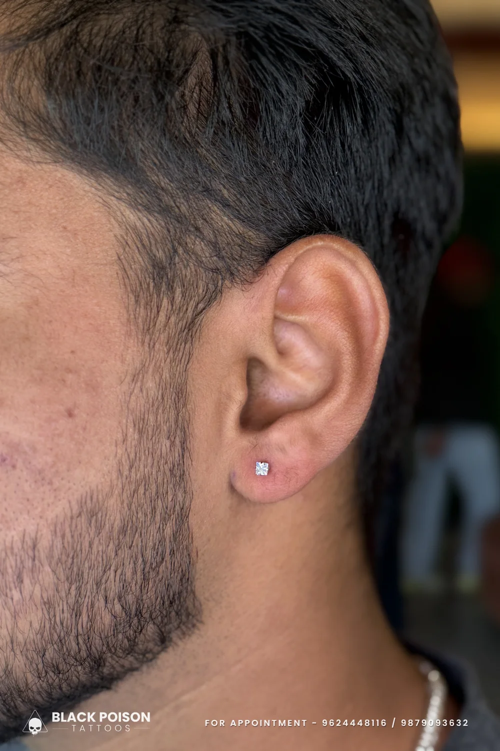 Men's ear lobe piercing with a small square crystal stud, a minimal and understated look on a fresh lobe piercing
